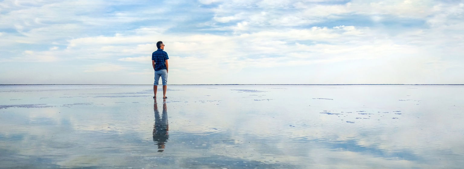 person at beach standing in water with reflection showing